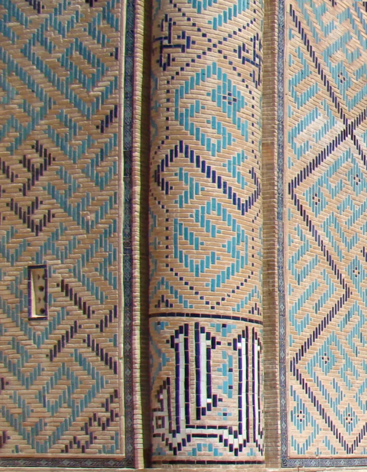 Architectural brickwork in the bannā'ī technique, where glazed and unglazed bricks form angular square-Kufic lettering on a wall.