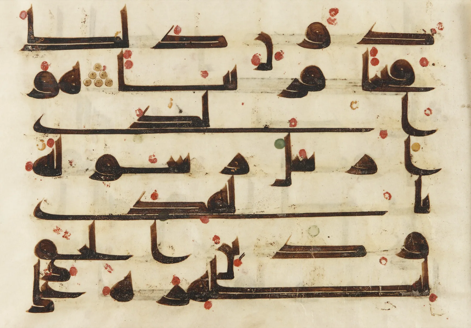 A parchment folio from an eighth or ninth century Qur'an in early Kufic script, with wide horizontally-extended letterforms in brown ink and sparse markings.